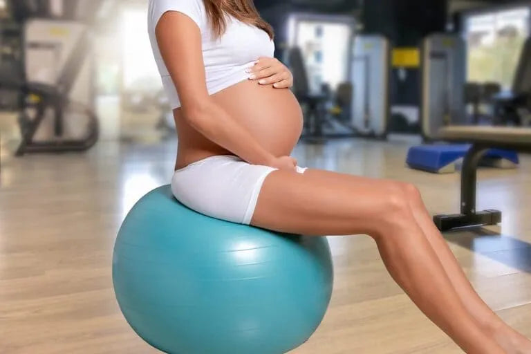 ballon de grossesse pour accoucher : femme enceinte en tenue de sport assise sur ballon d'accouchement bleu